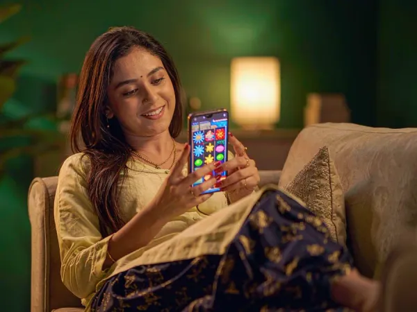 m444 Woman relaxes on a plush sofa with a smartphone showing a colourful slot game