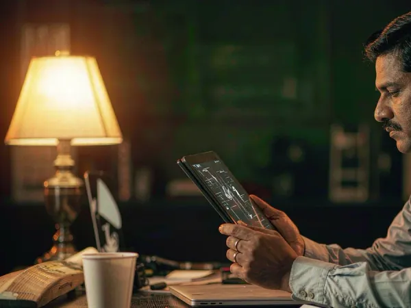m444 Man studies a match-data interface on a tablet beside a cricket bat and coffee