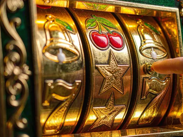 m444 Close-up of illuminated slot reels with cherries, bells and stars beside a hand on the button
