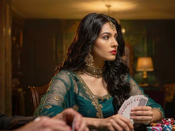 m444 Woman in teal and gold holds cards at a poker table stacked with chips