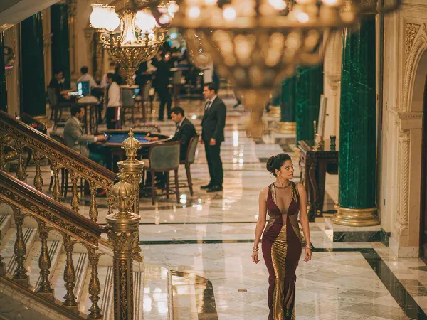 m444 Woman in a maroon and gold dress walks through a chandelier-lit casino lobby